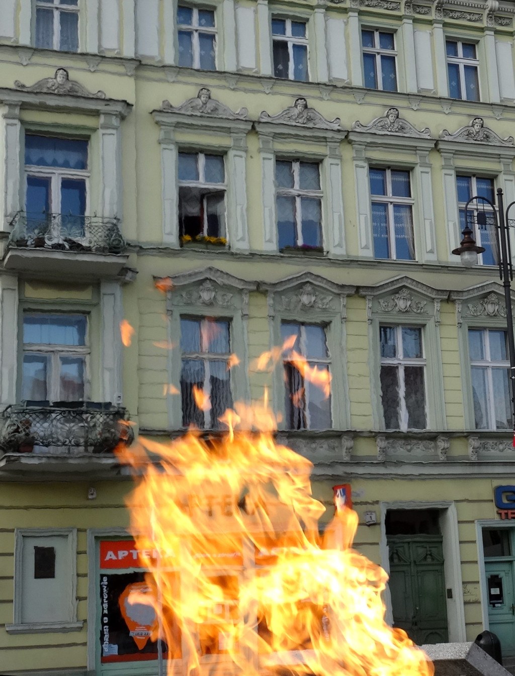 Großer Brand vor einem Gebäude mit Fenstern, Türen, einem Lichtmast und einer Tafel.