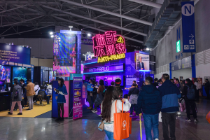 Eine große Gruppe von Menschen steht vor einem Stand auf einer Messe, einige halten Taschen, und Schilder mit der Aufschrift "Indie Game Development Award 2019".