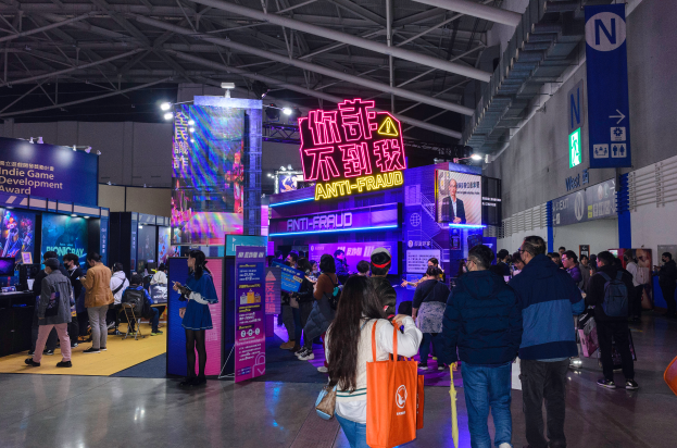 Eine große Gruppe von Menschen steht vor einem Stand auf einer Messe, einige halten Taschen, und Schilder mit der Aufschrift "Indie Game Development Award 2019".