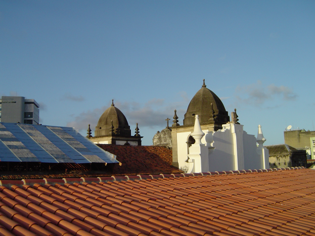 Eine Stadtansicht mit Gebäuden im Vordergrund und einem blauen Himmel im Hintergrund, die Solarpanels auf dem Dach eines Gebäudes zeigt.
