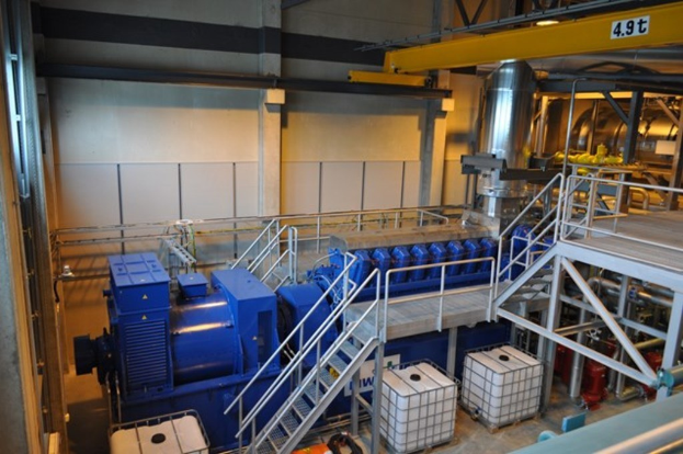 Eine Fabrikinnensicht mit Tr"gern, einer Treppe, Gel"ander, Containern, Lichtern, Rohren und W"anden.