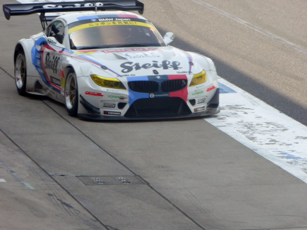 Ein strahlend blauer und weißer BMW Z4 GT3 Rennwagen mit großen glänzenden Felgen auf einer Rennstrecke.
