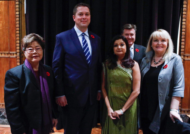 Gruppe von Menschen vor schwarzem Vorhang mit Holzwand im Hintergrund, die scheinbar Mitglieder der Liberalen Partei bei einer Versammlung sind.