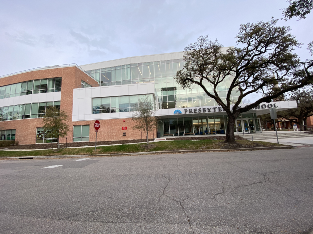 Presbyter Middle School, ein großes Gebäude mit vielen Fenstern, umgeben von Bäumen, Gras, Schildern, Pfosten und einer Straße, mit einem bewölkten Himmel im Hintergrund.