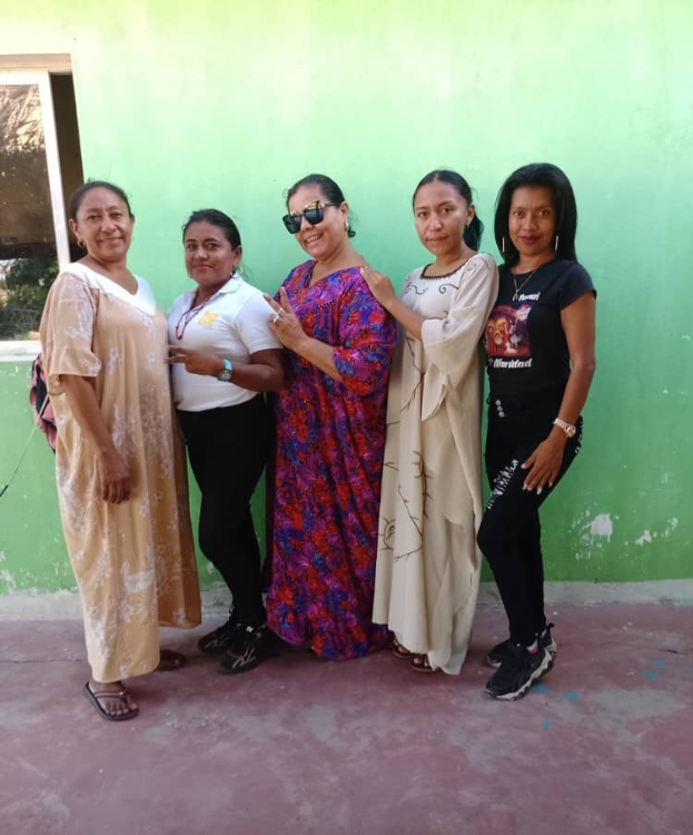 Eine Gruppe von Frauen, die vor einer grünen Wand mit einem Fenster auf der linken Seite stehen und an einem Internationalen Frauentag teilnehmen.