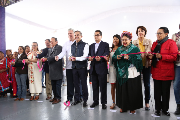 Gruppe von Menschen bei einer Scherenschnitte-Zeremonie, die vor einer Menge mit Papieren auf dem Boden und einem weißen Tuch im Hintergrund stehen.