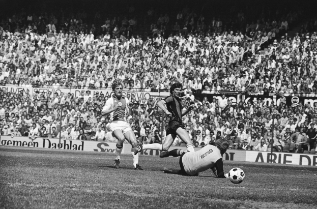 Schwarzes Foto von Männern beim Fußballspielen auf einem Feld mit Zuschauern im Hintergrund und einer 'Bundesliga 1978-79 Ajax 1-1 Hannover 96'-Tafel.