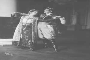 Schwarz-weiß-Foto eines Mannes und einer Frau, die in einem Ballsaal tanzen, mit einer Säule und einer Wand im Hintergrund; der Mann trägt Schuhe, was darauf hindeutet, dass sie eine Vorstellung geben.