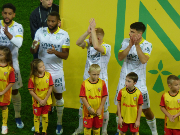 Eine Gruppe von Fußballspielern in Uniformen klatscht feierlich auf einem Ligue-1-Feld, mit einem "Ligue 1"-Schild im Hintergrund.