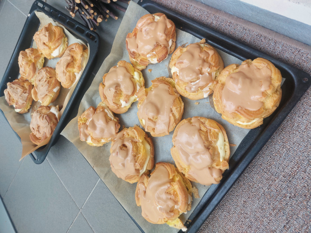 Ein Tablett mit verschiedenen Danish-Pasteten, einige mit Puderzucker bestäubt, steht auf einer Theke neben einem offenen Fenster und wird von warmem Licht beschienen.