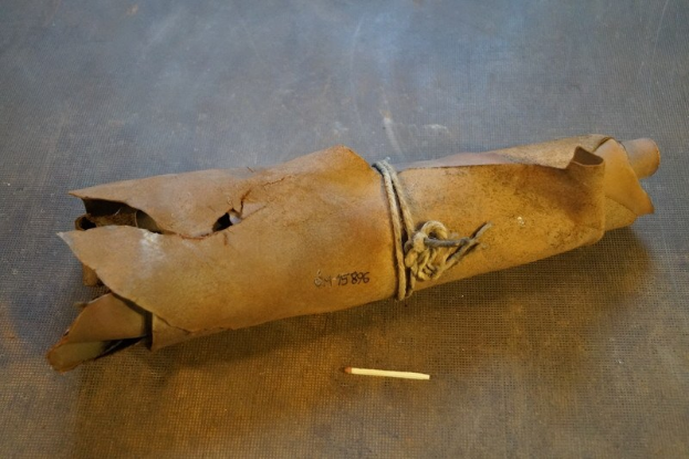 Ein brauner Papiertüte, die wie eine Granate aussieht, mit einem Seil daran gebunden und auf einem Tisch platziert, mit einer Zigarette daneben.