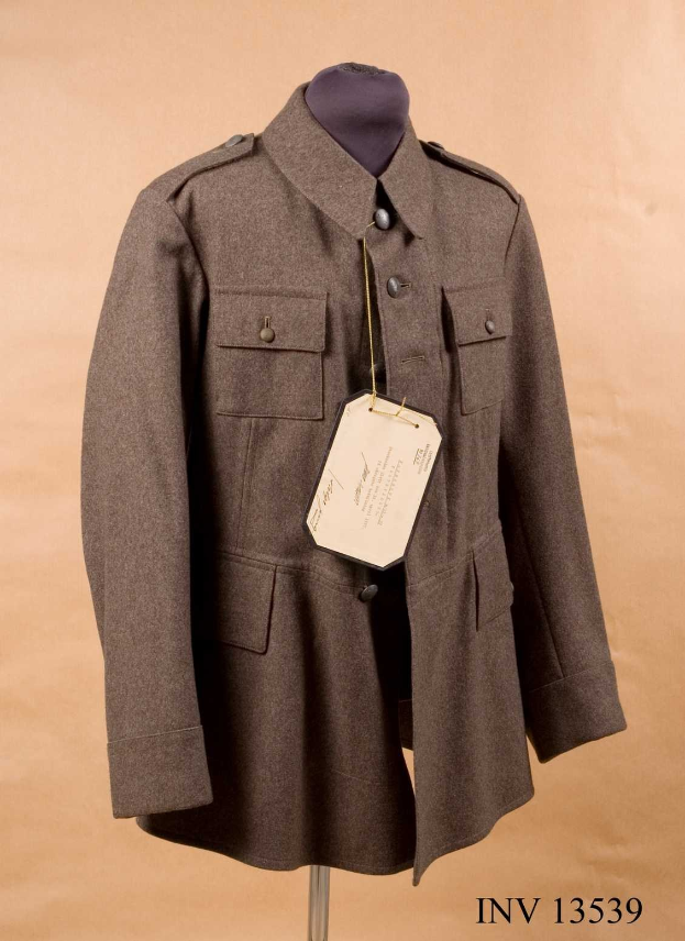 Luftwaffen-Offiziersjacke der deutschen Wehrmacht mit angebrachtem Schild, das auf einer Schaufensterpuppe gegen einen cremefarbenen Hintergrund gestellt wird, mit Text unten.