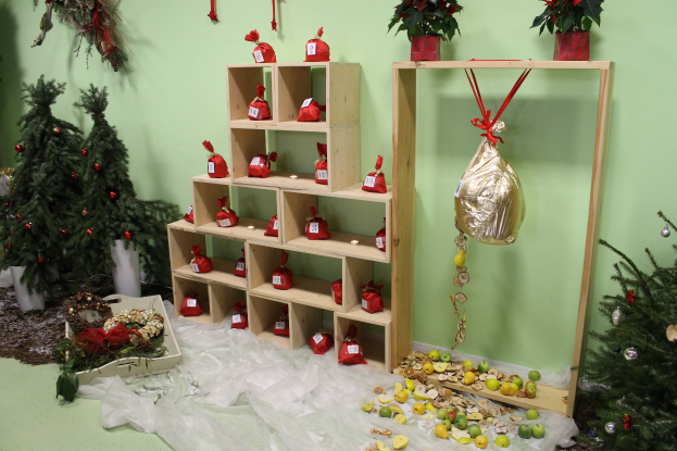 Ein Raum voller Weihnachtsdekorationen, darunter ein Weihnachtsbaum, ein Blumentopf, eine Schachtel, eine Abdeckung, einige Früchte, ein hölzernes Gestell mit Gegenständen, Topfpflanzen, Wanddekorationen und eine Gruppe von Weihnachtsbäumen.