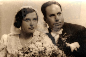 Ein Mann und eine Frau in festlicher Kleidung lächeln glücklich auf ihrer Hochzeit, die Frau hält einen Blumenstrauß.