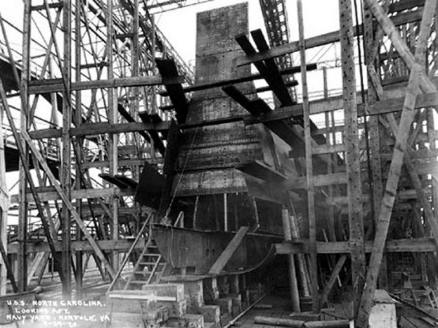 Schwarzes und weißes Foto eines Schiffs in einem Schiffbauhafen, mit hölzernen Pfählen und Treppen im Vordergrund und Himmel im Hintergrund, mit dem Text "Marinebewaffnung" in der linken unteren Ecke.