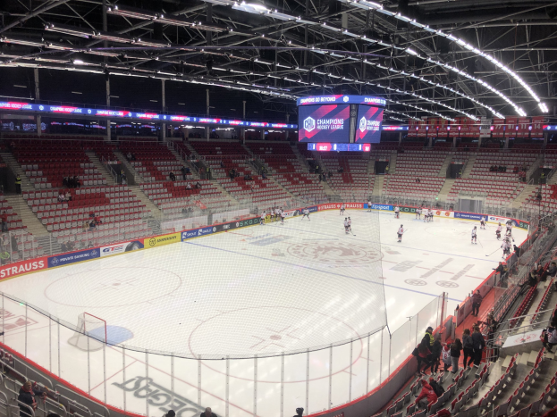 Hockey-Spiel in einer großen Arena zwischen den St. Louis Blues und Detroit Red Wings, mit Zuschauern auf den Sitzen und Stehplätzen in der Nähe der Eisfläche, umgeben von einem Zaun und Anzeigetafeln.