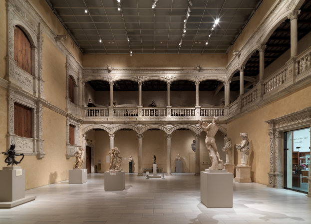 Große Museumsgalerie mit zahlreichen Statuen und Skulpturen auf Sockeln, architektonischen Elementen wie Wänden, Säulen, Geländern und einer beleuchteten Decke, mit einigen Besuchern.