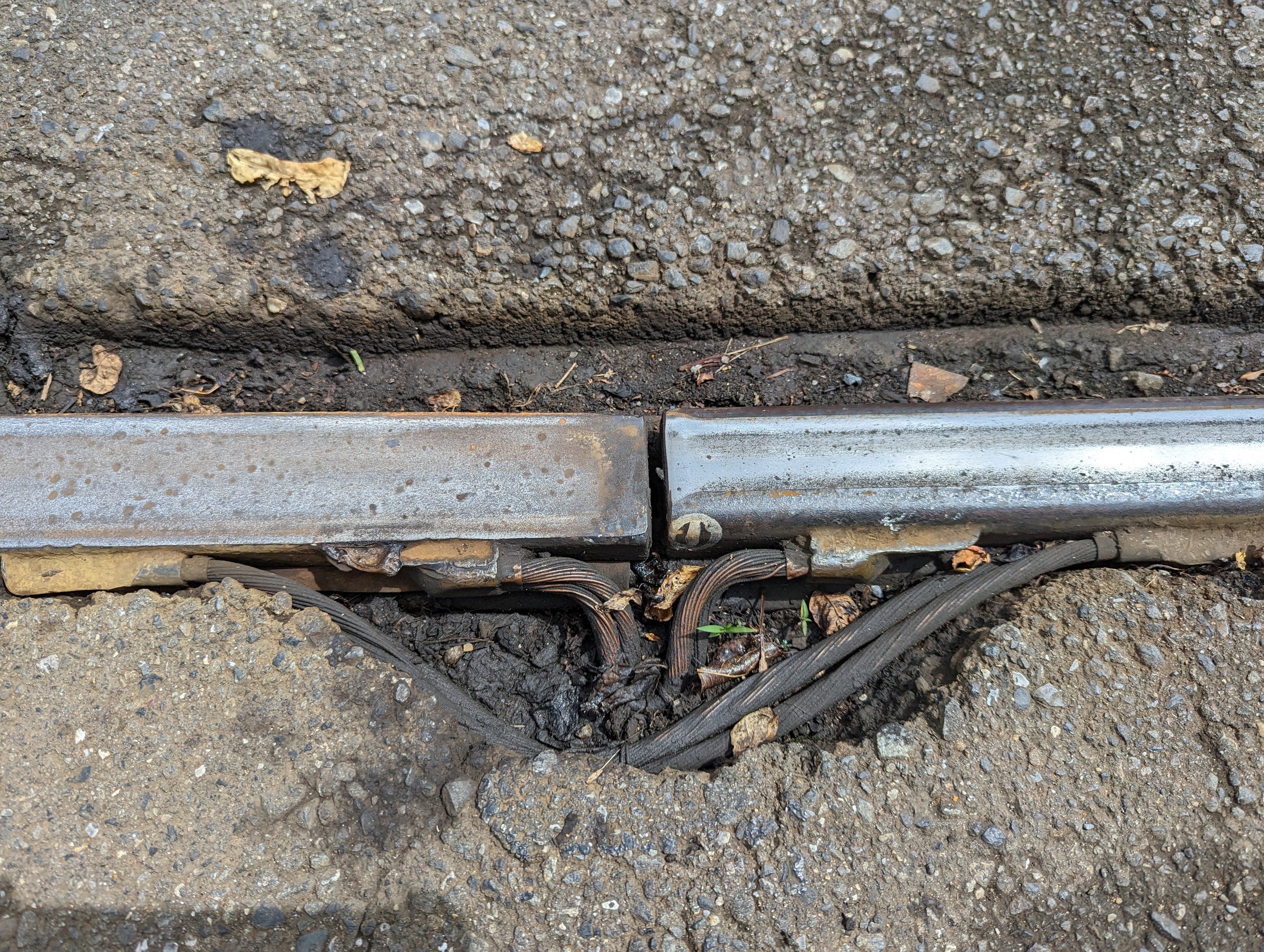 Nahaufnahme eines Metallkanals auf der Straße mit angeschlossenen Drähten und verstreuten trockenen Blättern.