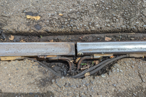 Nahaufnahme eines Metallkanals auf der Straße mit angeschlossenen Drähten und verstreuten trockenen Blättern.