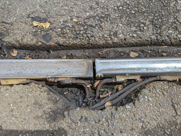 Nahaufnahme eines Metallkanals auf der Straße mit angeschlossenen Drähten und verstreuten trockenen Blättern.